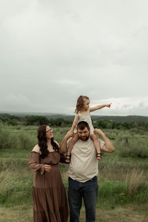 A couple stands together in a lush green field on an overcast day, sharing playful and candid moments together.