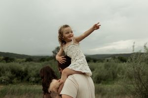 A couple embraces in a romantic outdoor setting with rolling green hills and cloudy skies in the background.