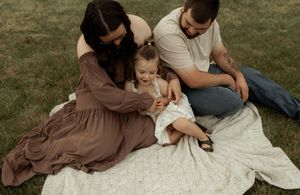 Family sitting together on a white blanket in grass during an outdoor photo session.