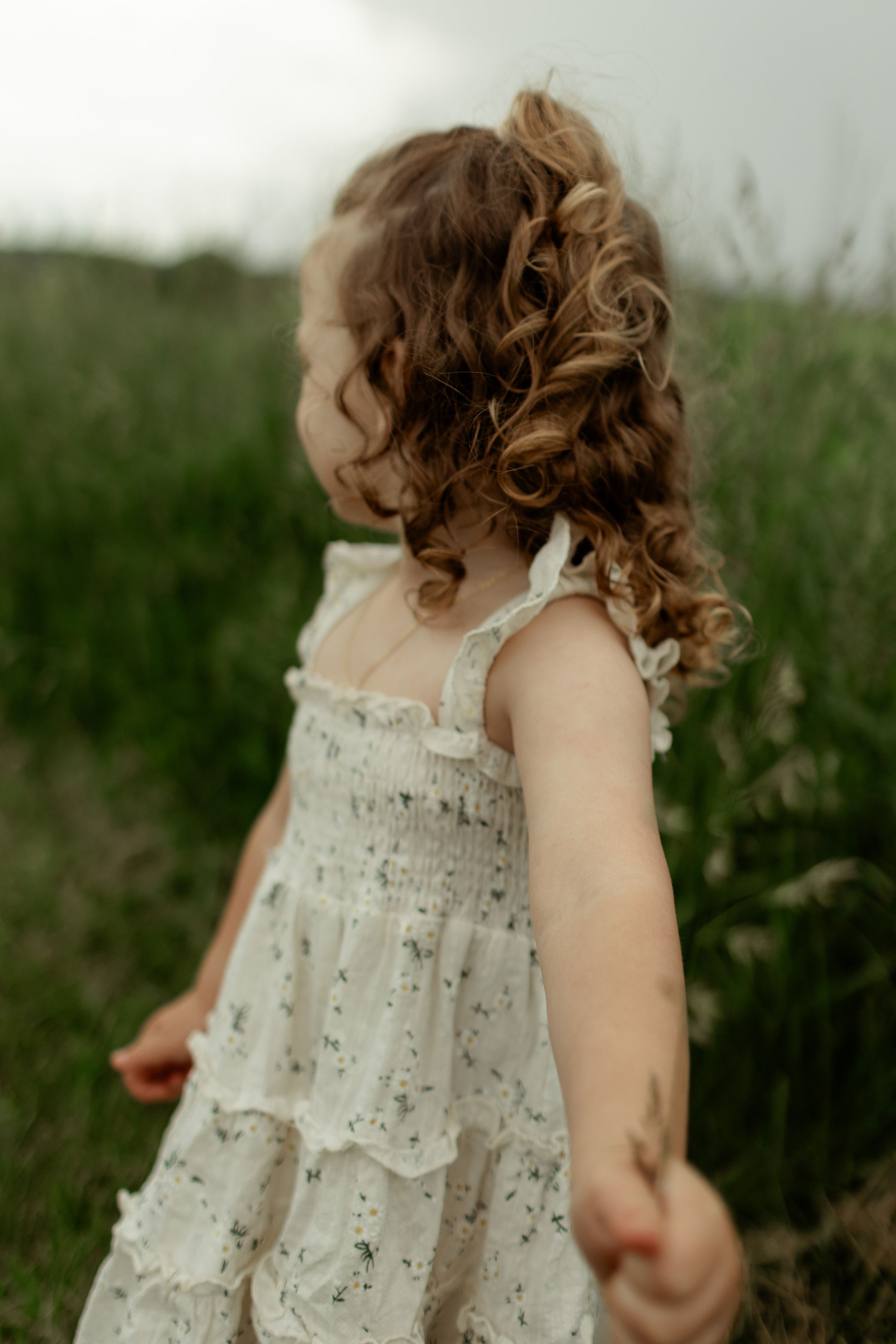 A child in a white lace dress runs through a green field on a summer day.