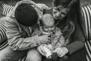 Black and white photo of parents lovingly holding their newborn baby outdoors on a striped blanket.