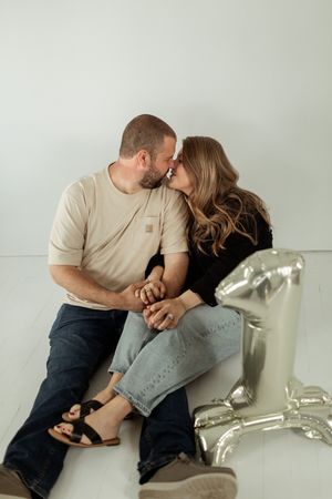A couple in casual clothing share an intimate moment against a light gray wall.