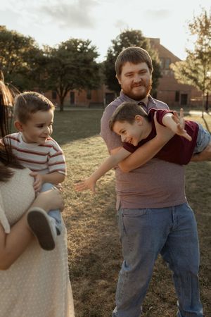 Family enjoying outdoor playtime at golden hour, father playfully holding children while mother watches warmly.