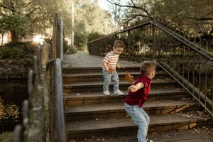 Two young boys playing on wooden steps near a railed bridge in a park during golden hour.