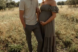 Couple posing in a field, pregnant woman in olive green off-shoulder maxi dress with partner in matching tones.