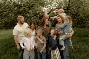 Large family gathering outdoors under blooming trees, smiling adults and children enjoying a portrait in a lush green meadow.