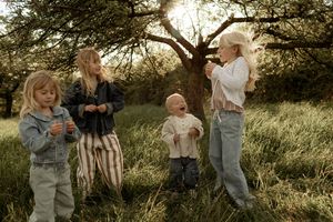 Four blonde children playing with bubbles in a sunlit meadow with a large tree in the background.