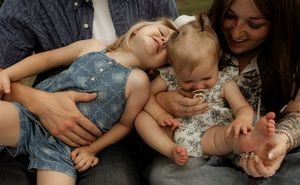 Two young children laughing and playing on laps of adults during a casual family photo session outdoors.