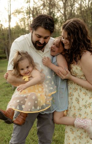 Happy family of four sharing a joyful outdoor moment, parents smiling with two young daughters in a sunny green field.