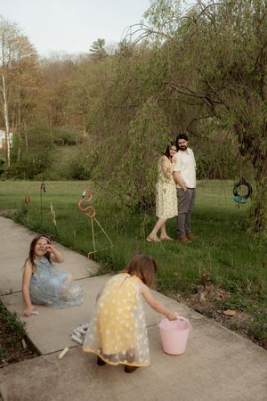 A family of four enjoys a spring afternoon outdoors, with parents watching their two daughters play on a garden path.