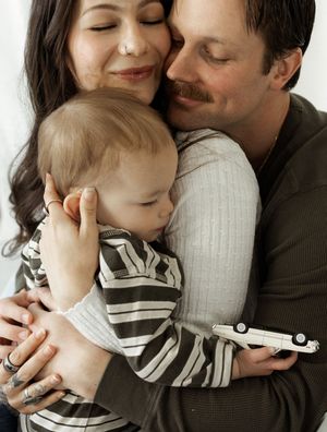 A loving family moment as parents embrace their baby, who holds a toy car, in a warm and tender portrait.