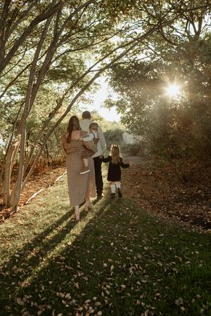 A family walks together on a sunlit forest path during golden hour as sunbeams filter through the trees.