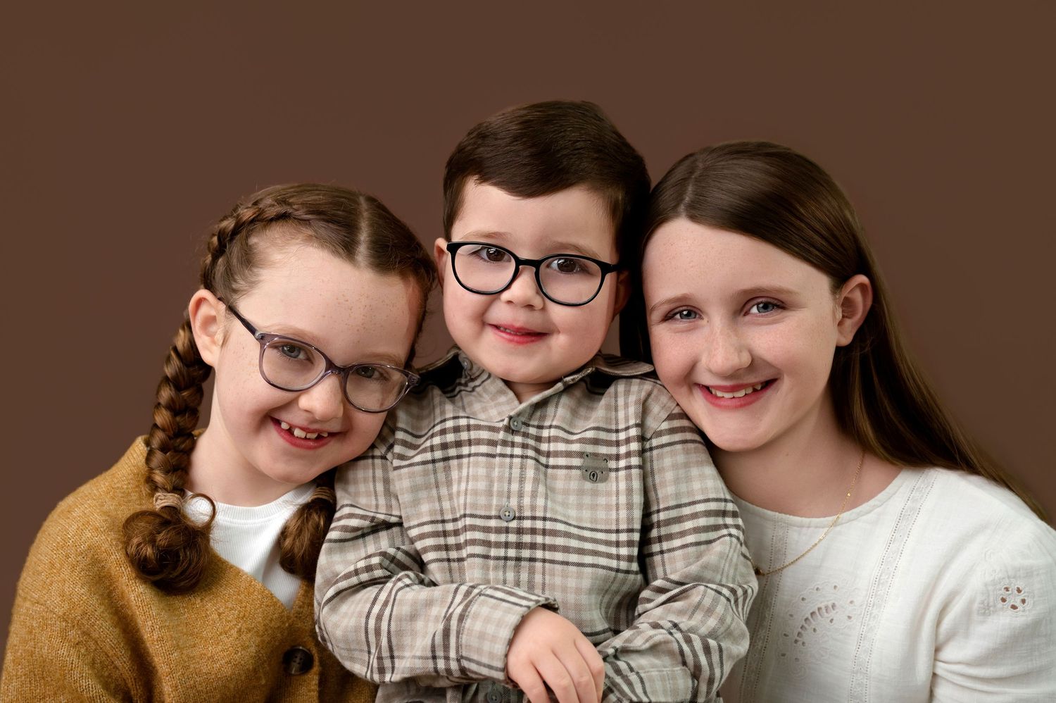 Three smiling people wearing glasses pose together for a casual family photo in warm brown tones.