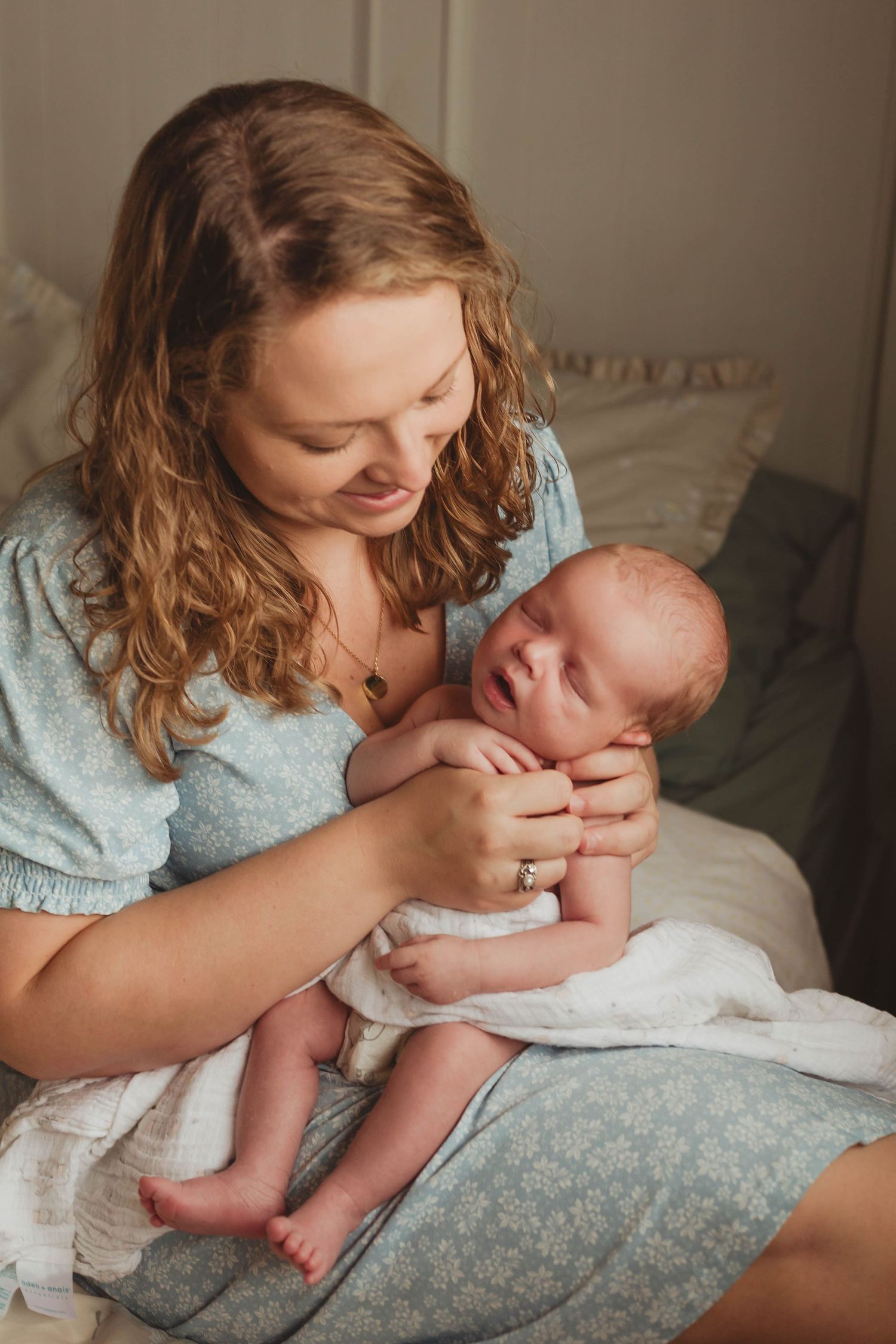A tender moment between mother and newborn baby during an intimate lifestyle photography session on soft bedding.