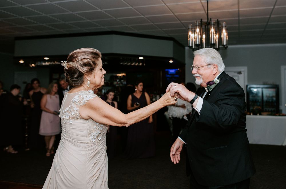 Wedding guests dance and celebrate on a dimly lit dance floor during an evening reception celebration.