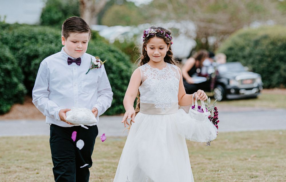 A wedding couple walks together outdoors surrounded by flower petals being tossed in celebration.