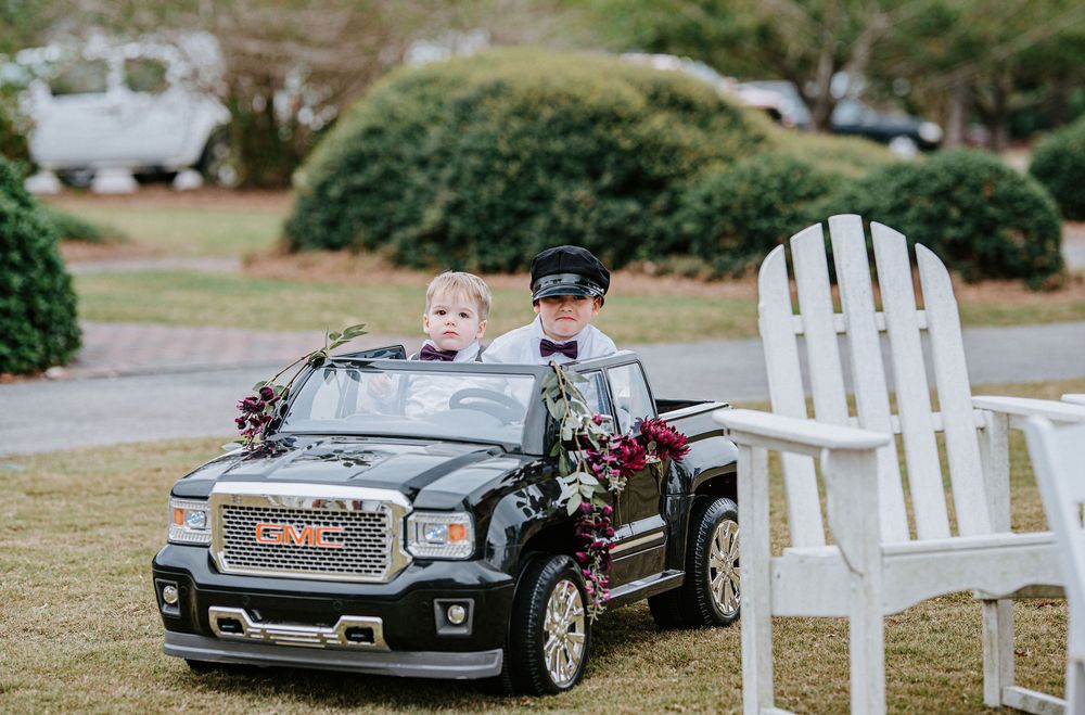 A collection of toy cars and white Adirondack chairs arranged outdoors in a garden setting.