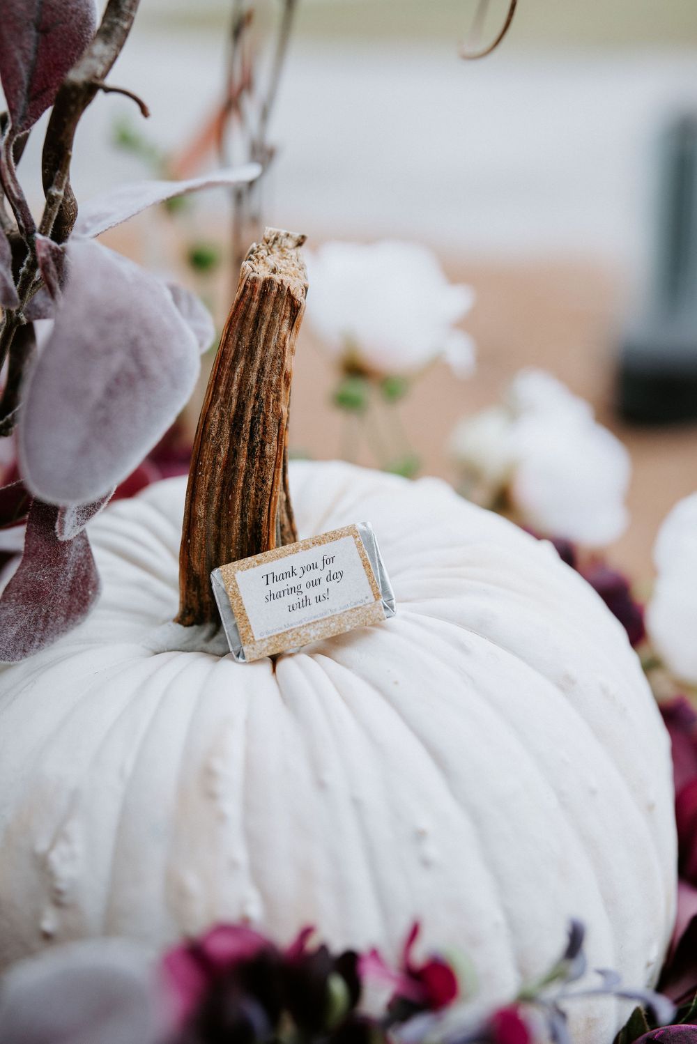White decorative pumpkins with burgundy floral accents create an elegant autumn display on a table.