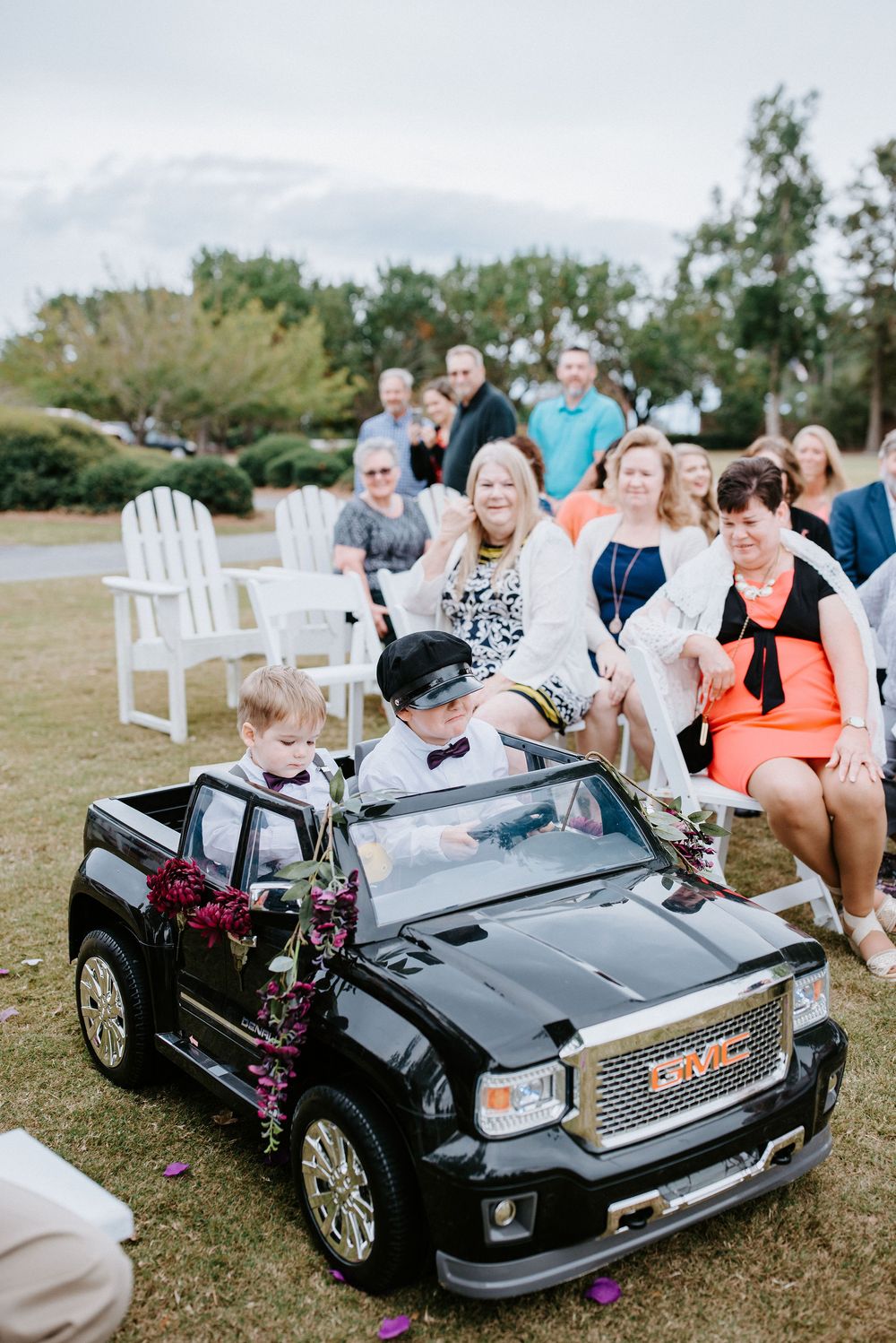 Small black toy electric car decorated with purple flowers parked on grass during an outdoor event.