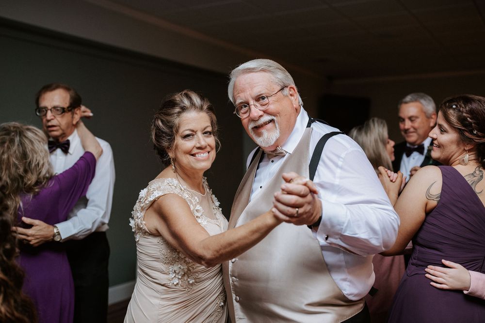 Wedding guests dance together on the dance floor at an indoor reception celebration.