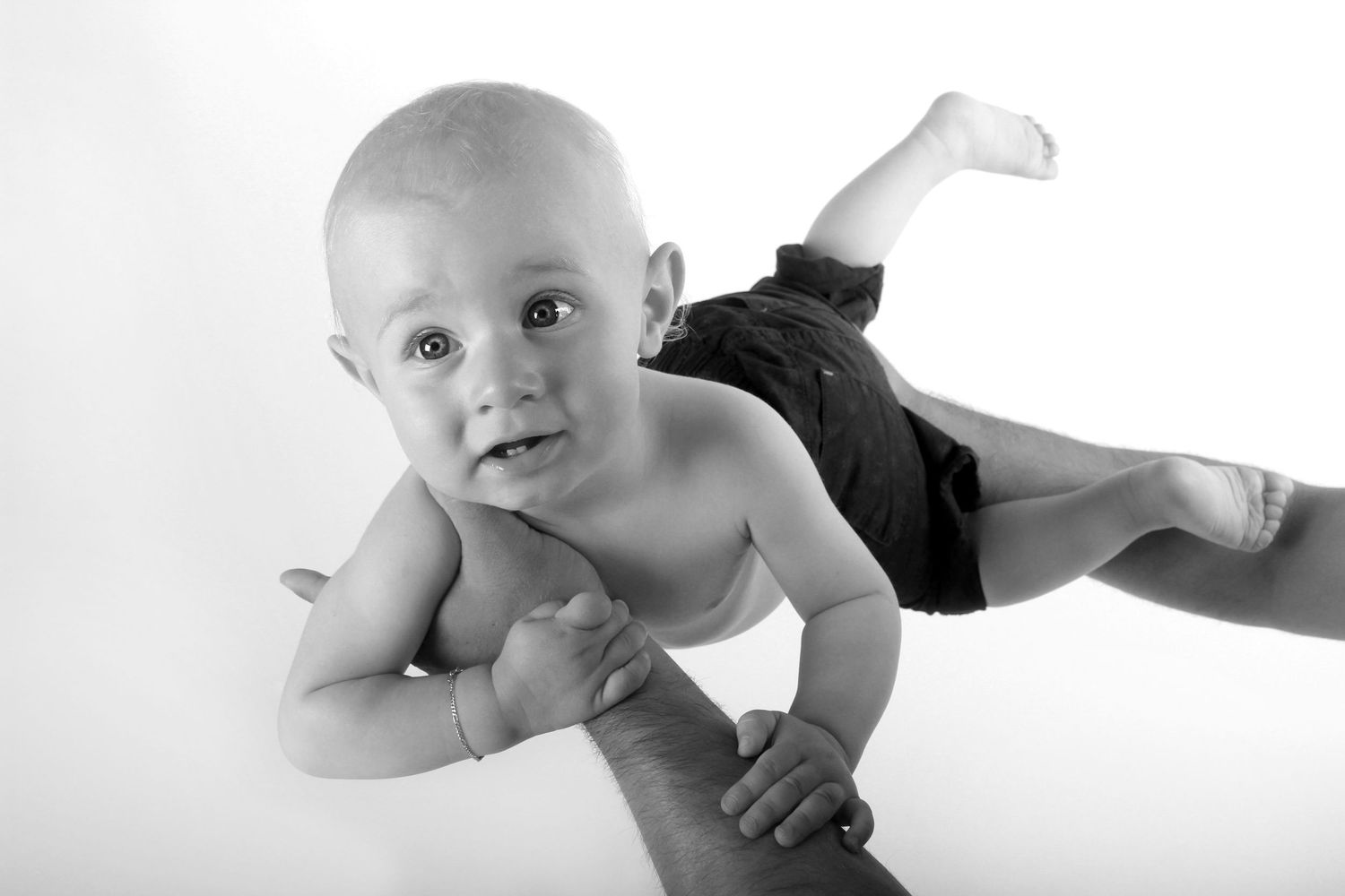 A black and white photo series shows a baby lying on their back in various playful poses on a white background.