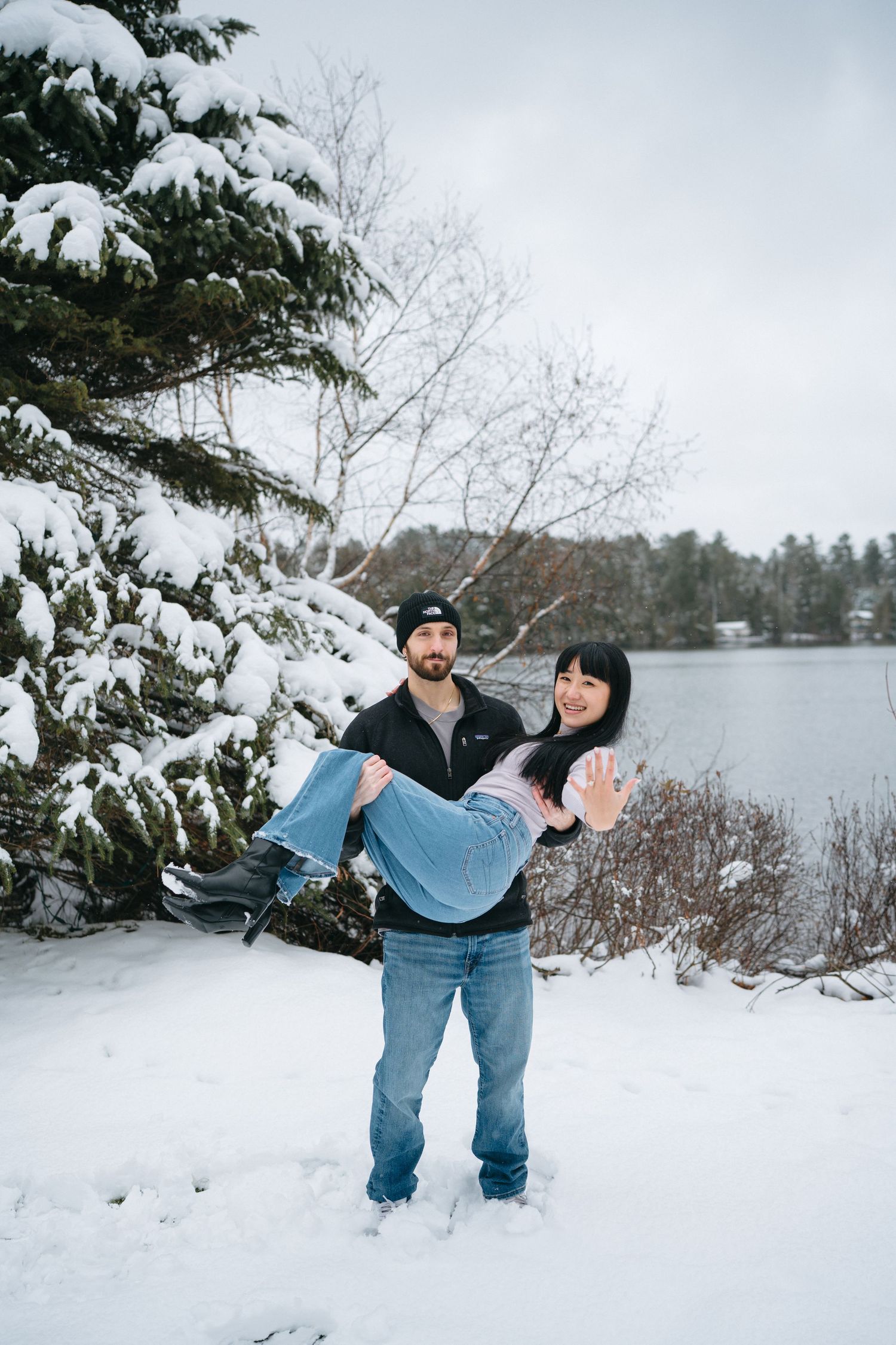 A playful winter scene with someone being carried in the snow near a lake.