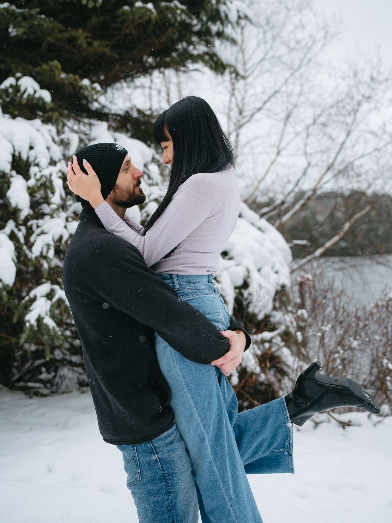 A playful couple embraces and lifts each other in the snow during a winter photoshoot.