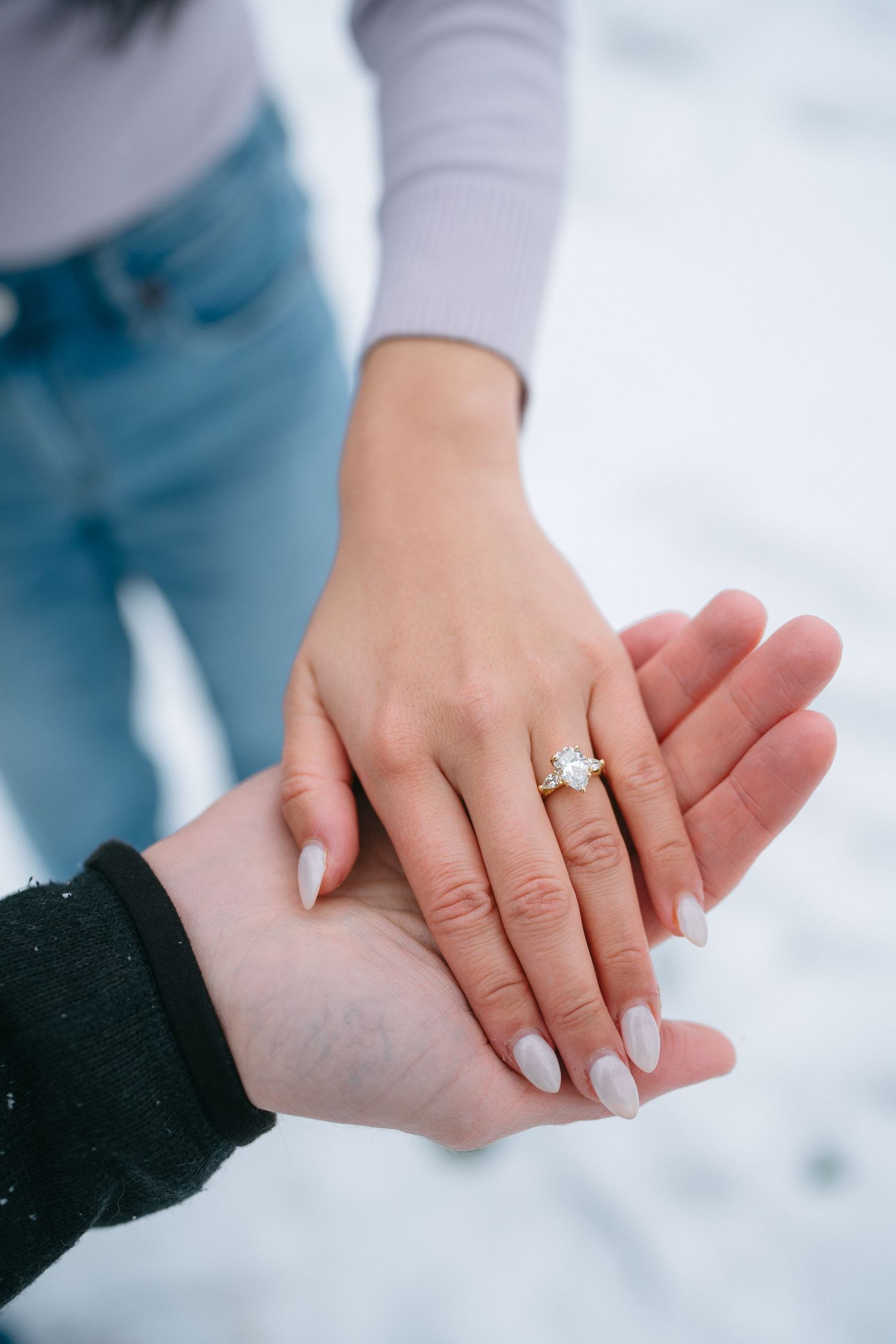 Close-up of hands showing off an engagement ring against a snowy winter backdrop.