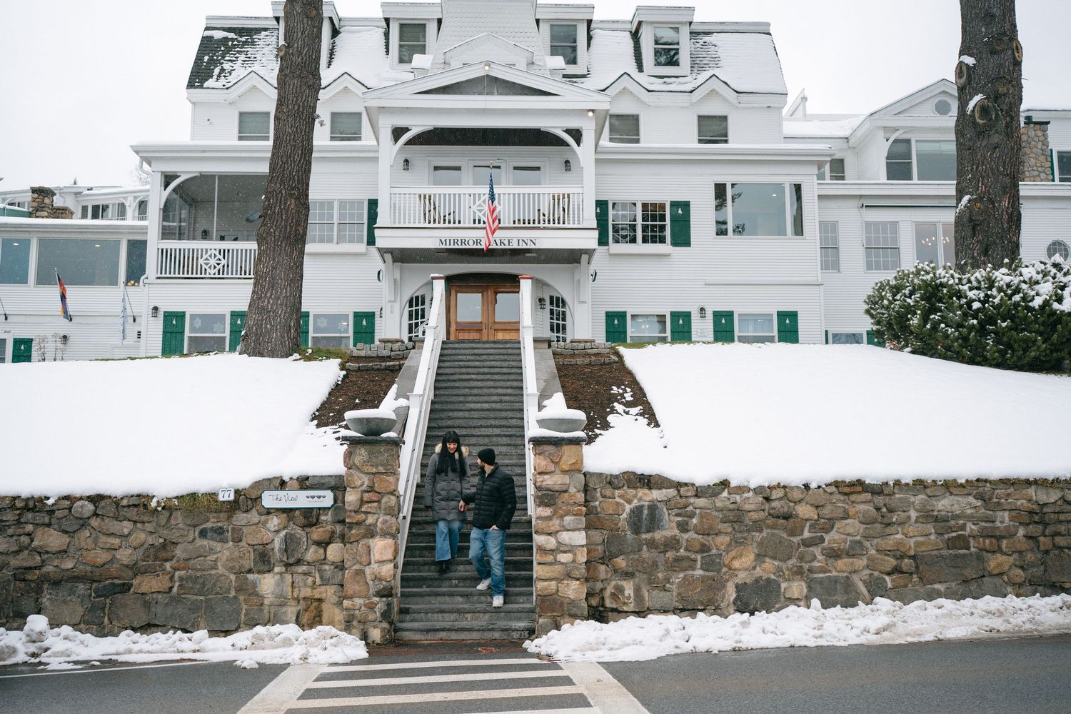 A row of elegant white coastal homes with green shutters behind a snow-covered stone wall.