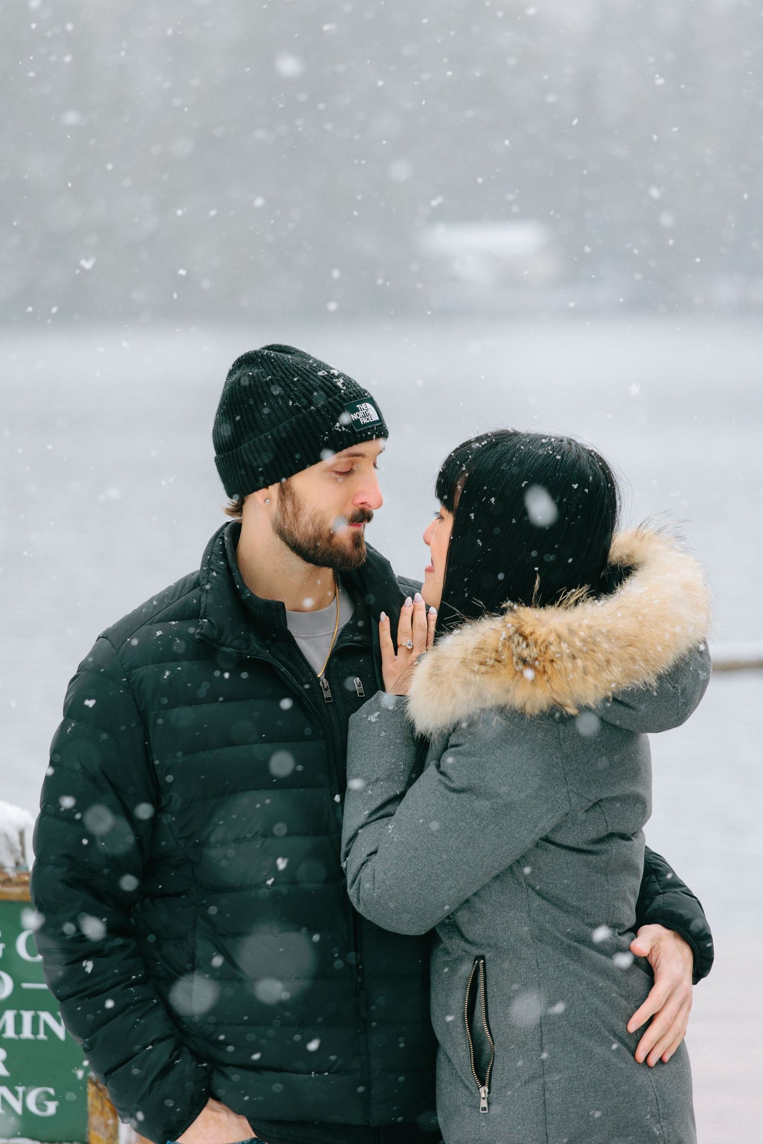 A romantic winter moment captured in the falling snow with two people in warm coats and winter hats.