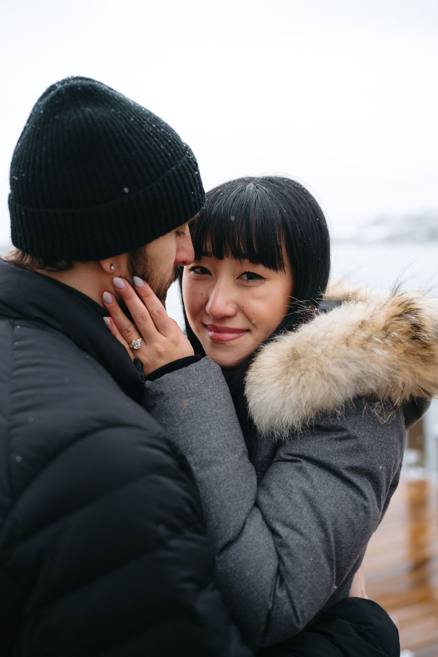 An intimate moment shared between a couple wearing matching gray winter coats on a wooden deck.