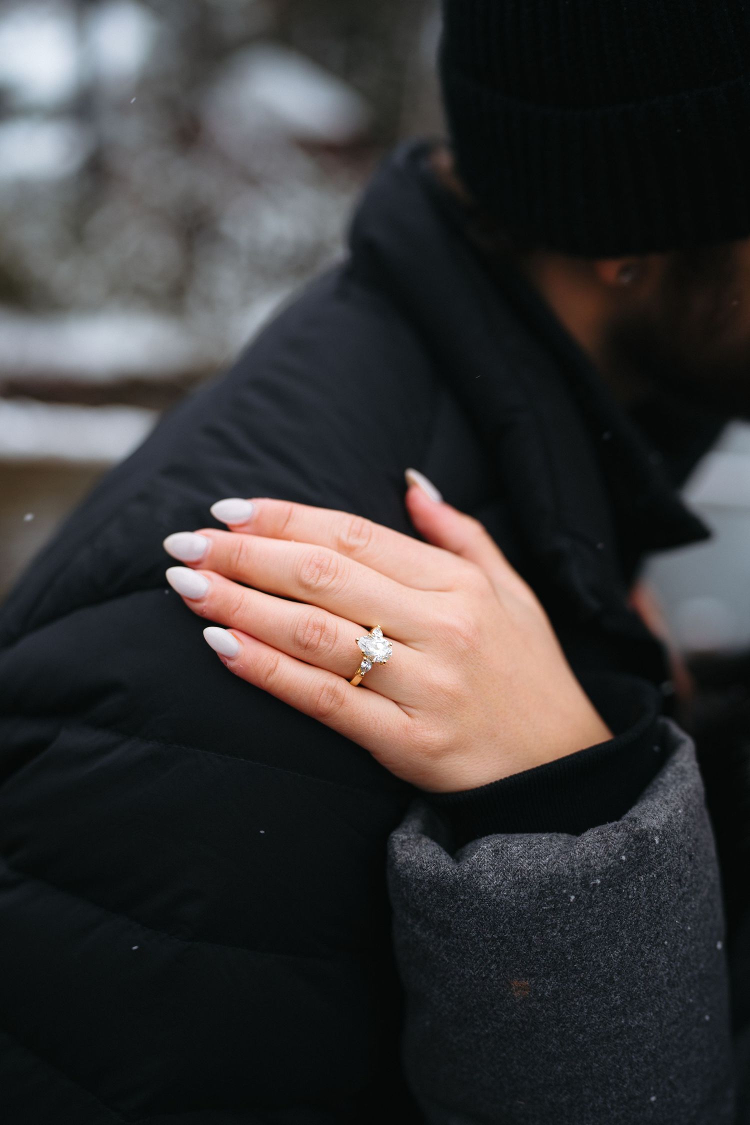 A close-up shot of a hand wearing an engagement ring against a black sleeve.
