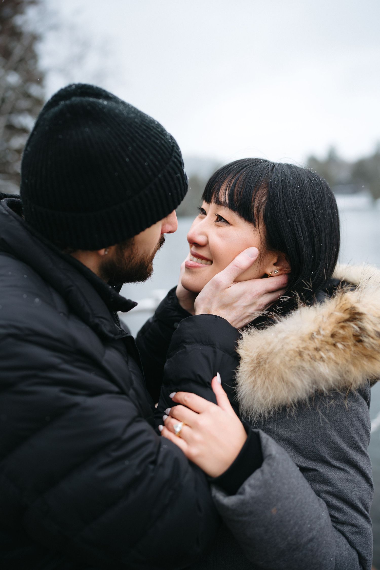 A tender winter scene of a couple embracing outdoors, with one wearing a fur-trimmed coat and the other in a beanie.