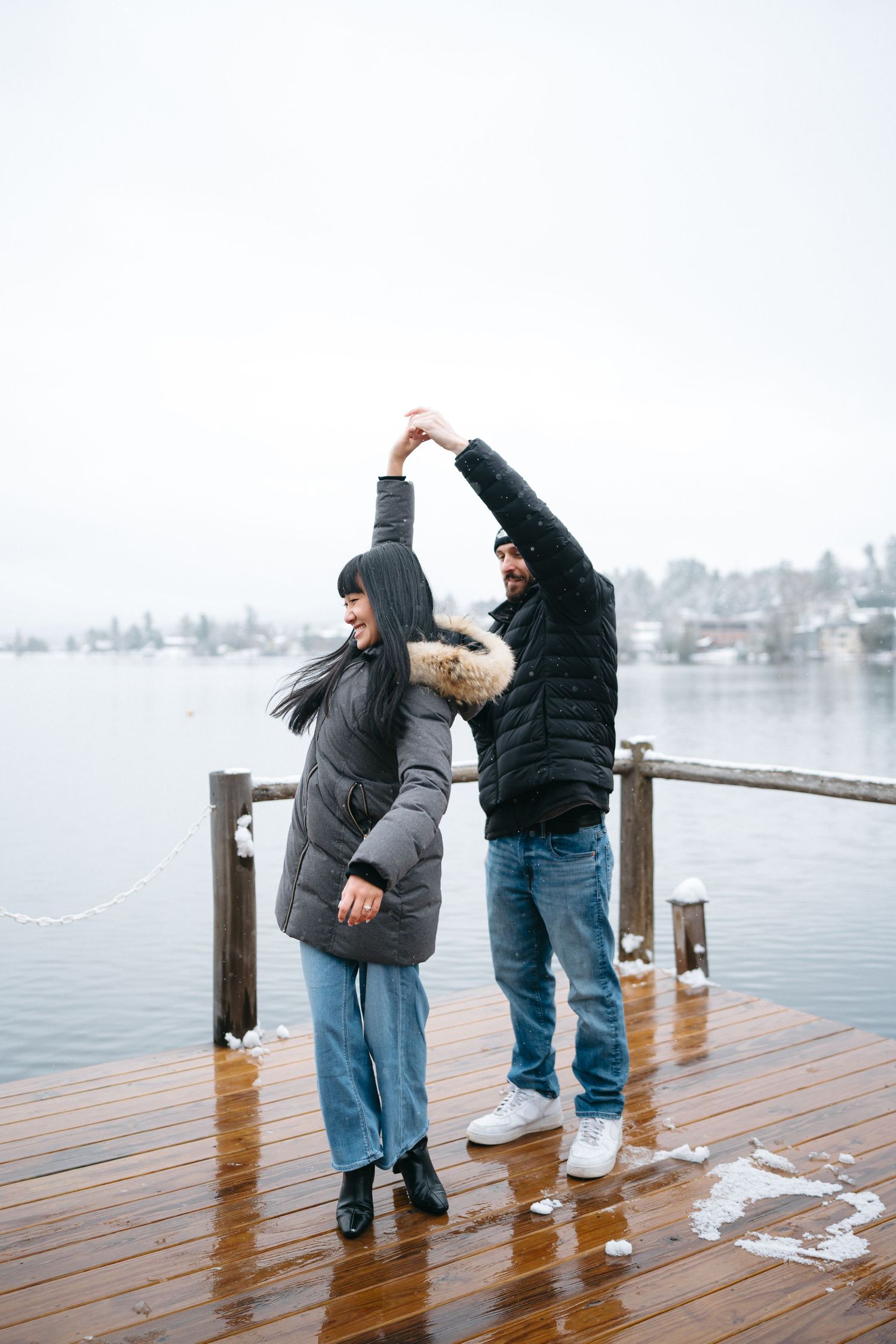 Two people share a romantic moment on a wooden dock by a lake in winter.