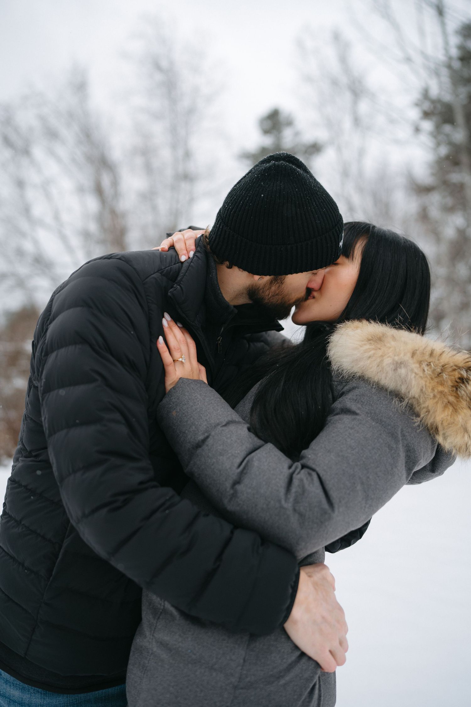 Intimate embrace between couple in winter coats during a snowy day.