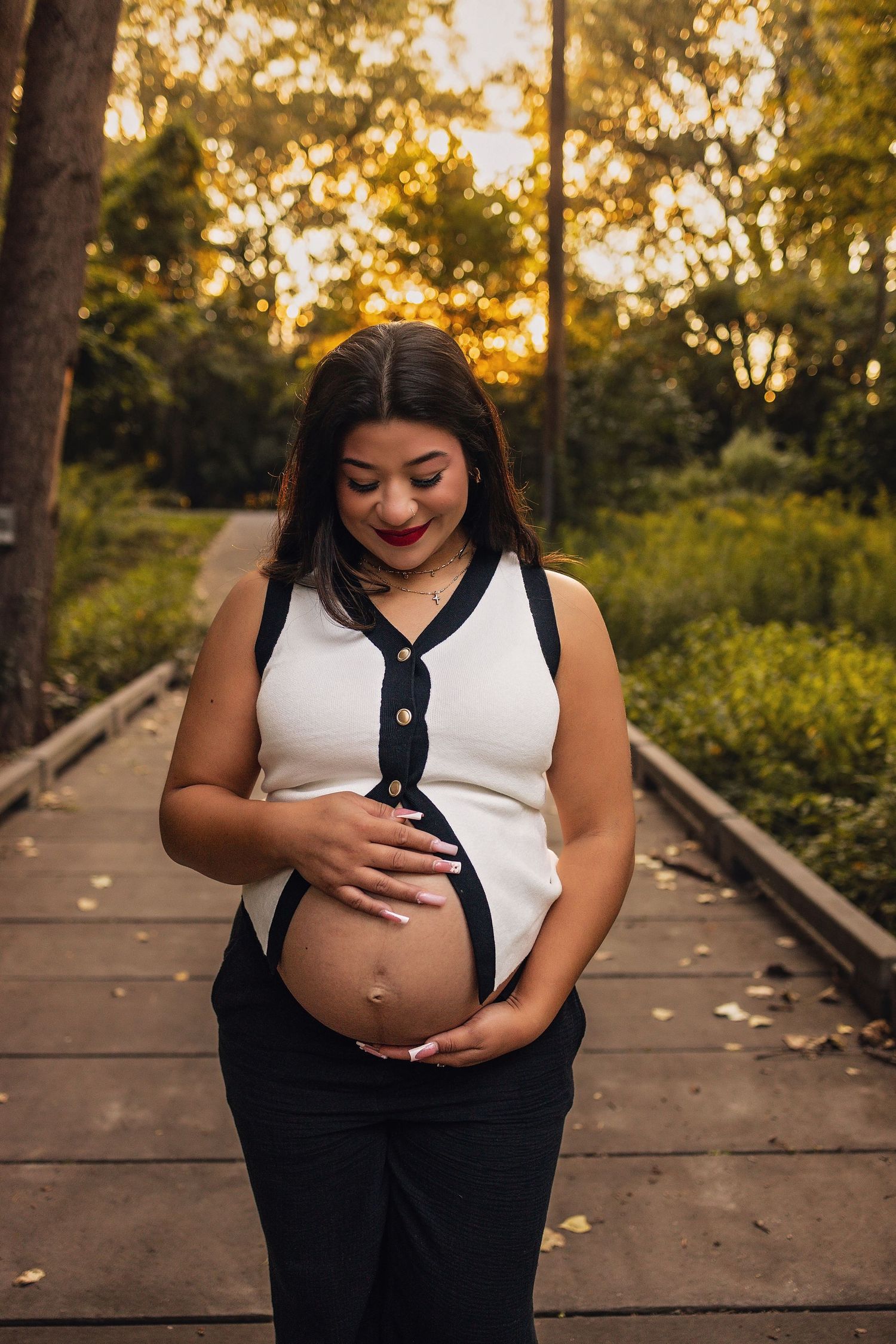Maternity photo of an expectant mother in a white top standing on a wooden boardwalk at sunset.