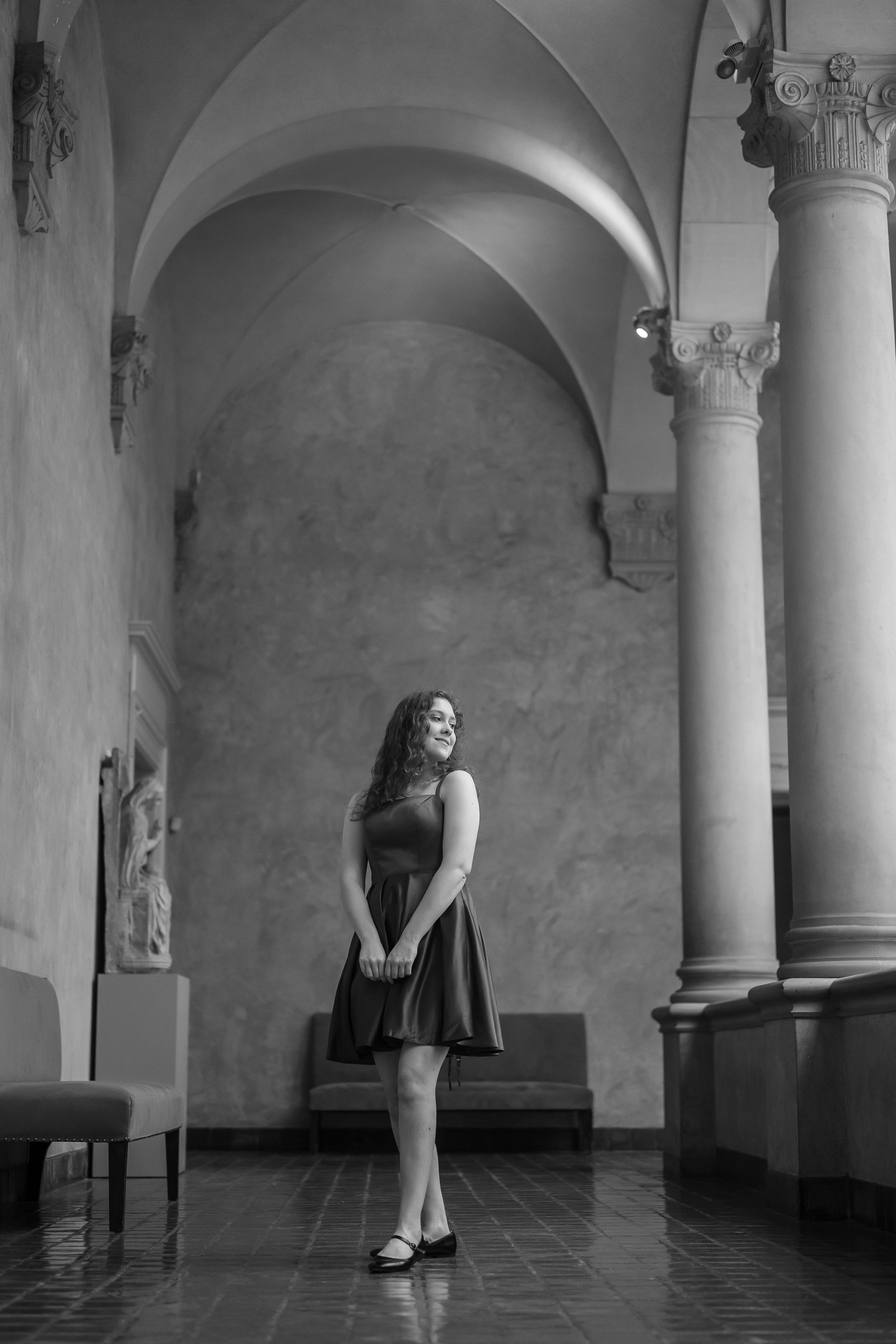A black and white photo series showing a woman in a dress standing in an arched hallway with columns.