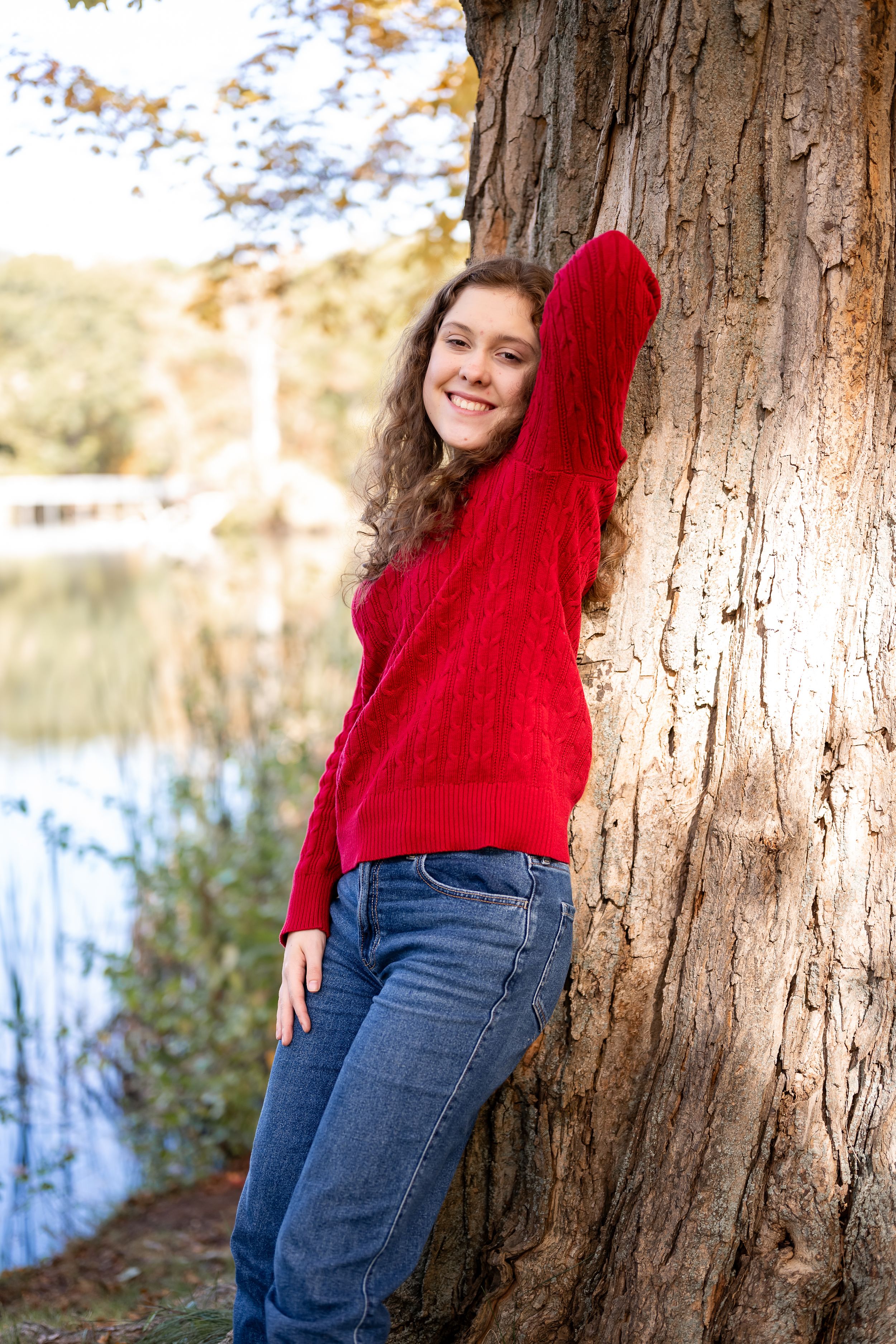 A casual outdoor portrait against a tree trunk features someone in a cozy red sweater and denim jeans.