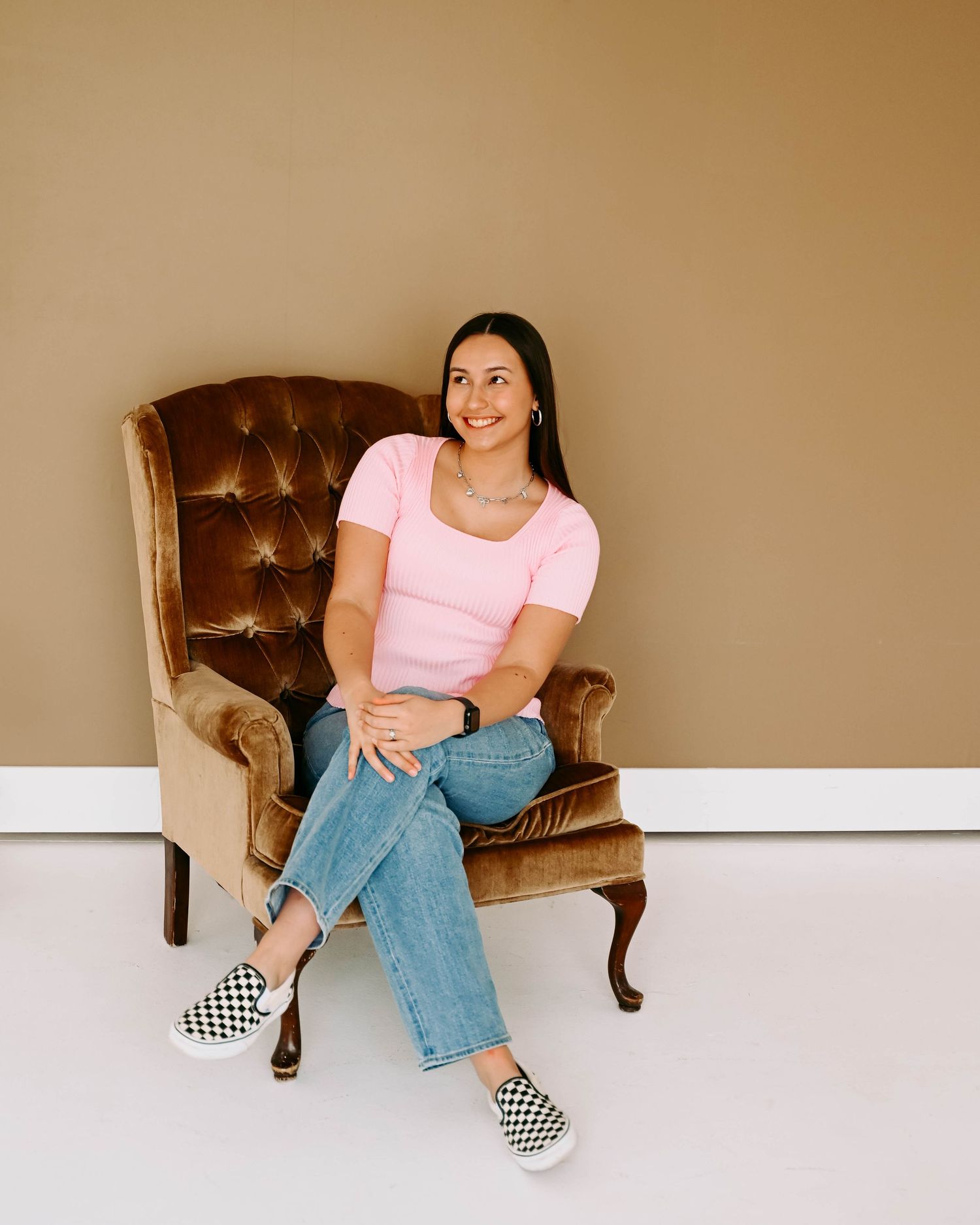 Person in pink t-shirt and jeans lounging casually on brown leather chair wearing checkered slip-on shoes.