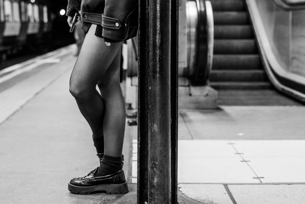 Low angle black and white view of someone leaning on the train platform wearing dress shoes.