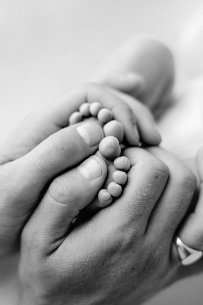 A black and white macro photographs showing parents hands holding on to newborn baby feet.