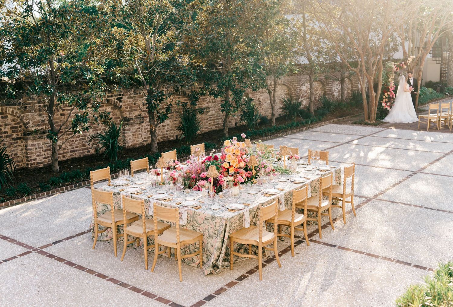 Rustic outdoor wedding reception setup with wooden chairs and tables arranged in rows on a stone patio.