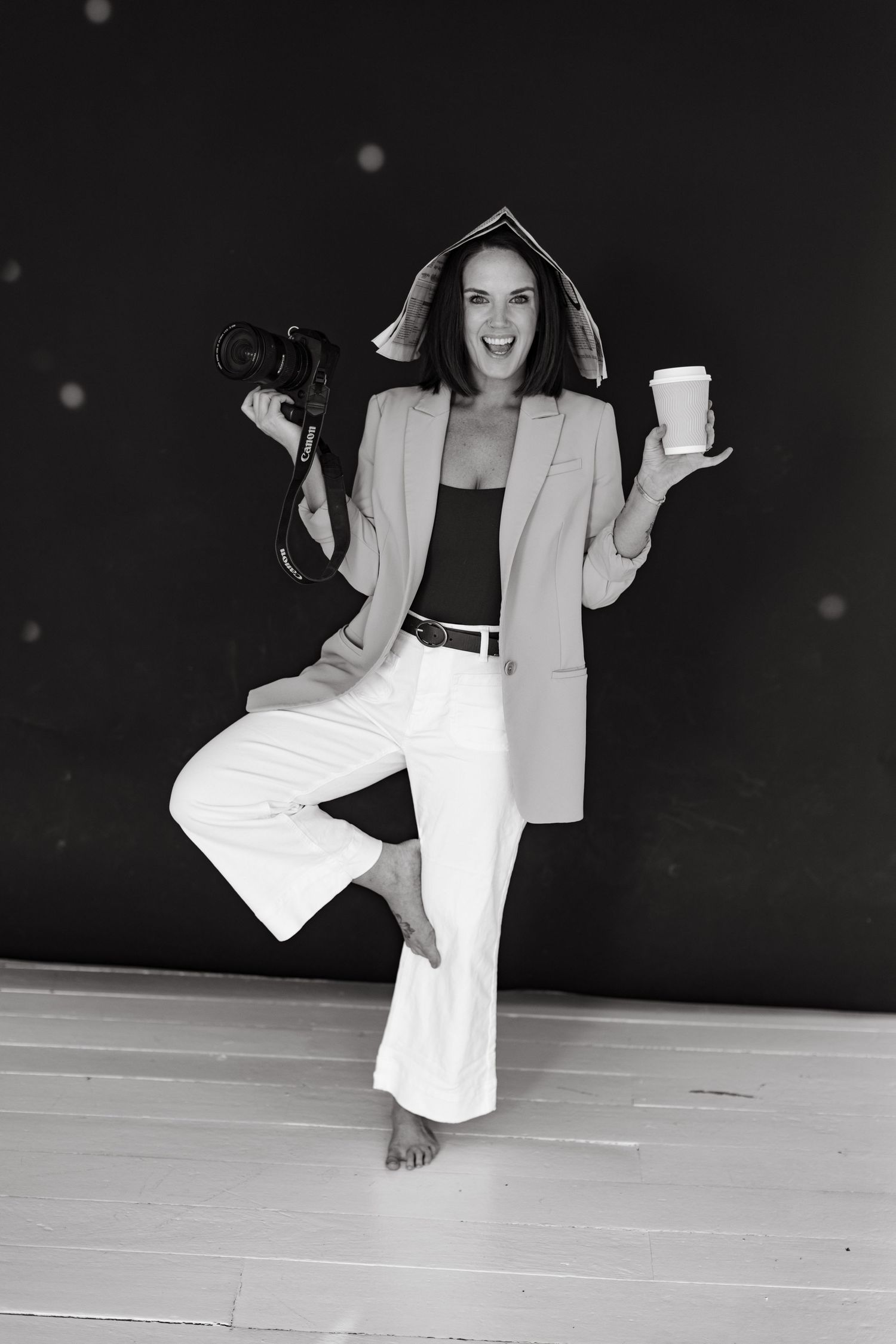 Black and white photo of a woman in white blazer sitting playfully on a stage.