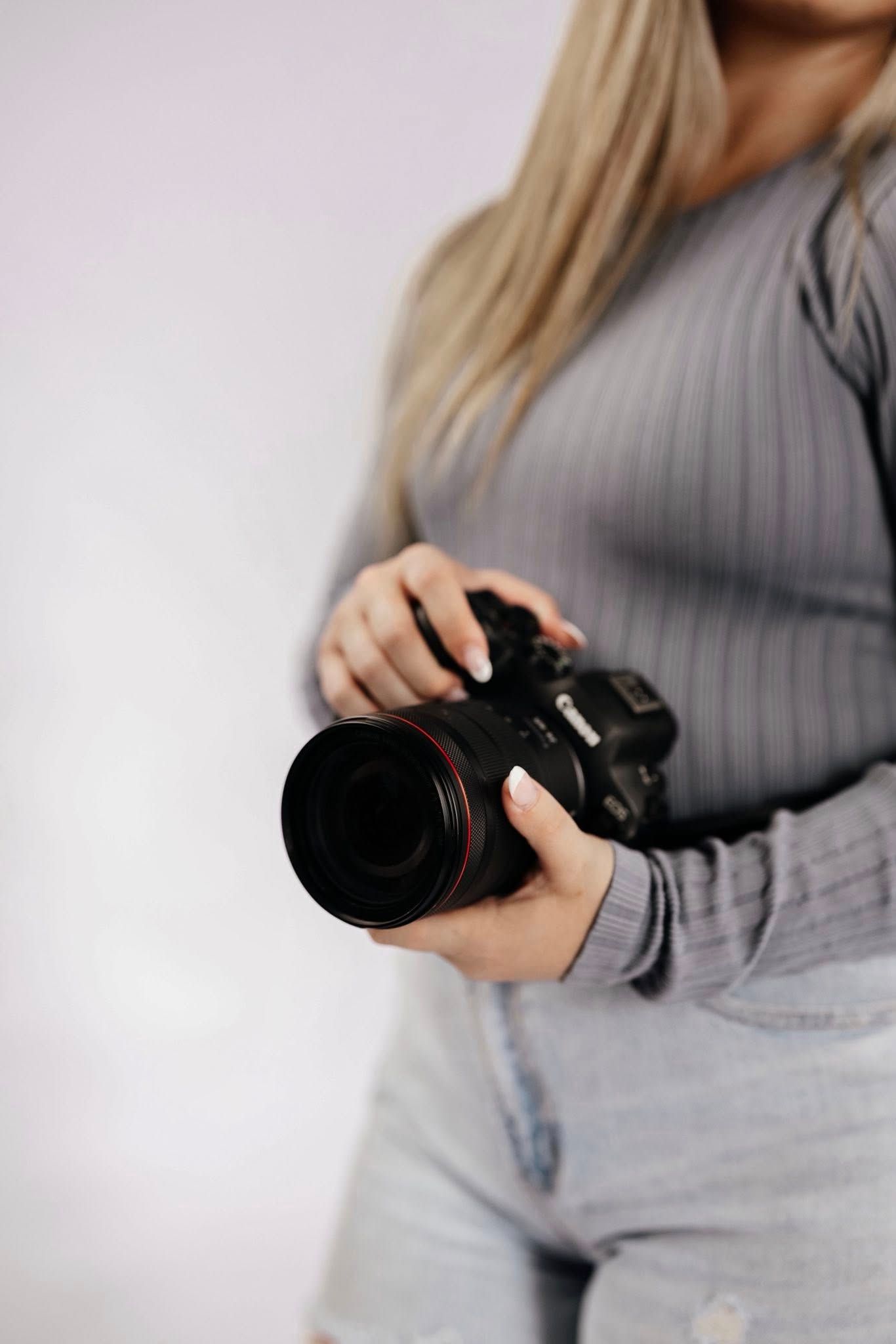 Close-up of female photographer holding professional DSLR camera with red-ring lens.