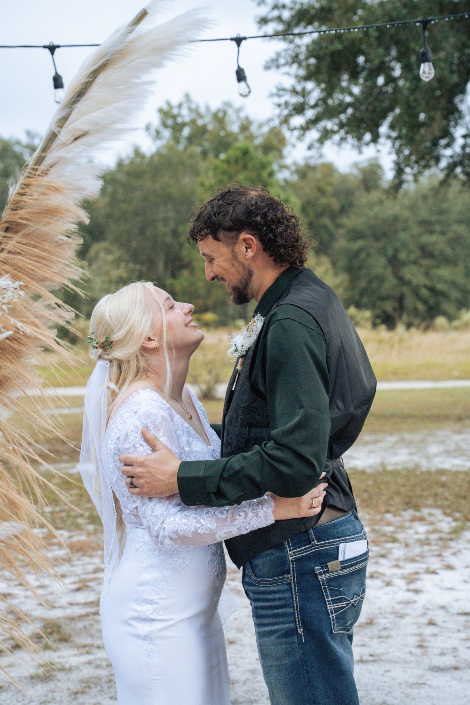 A couple shares an intimate moment in a snowy field with trees in the background and string lights overhead.