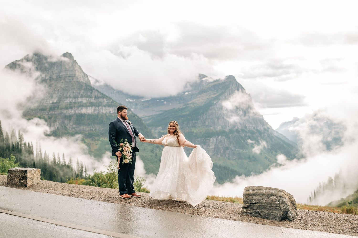 A couple poses for wedding photos in front of misty mountain peaks at a scenic overlook in the Canadian Rockies.