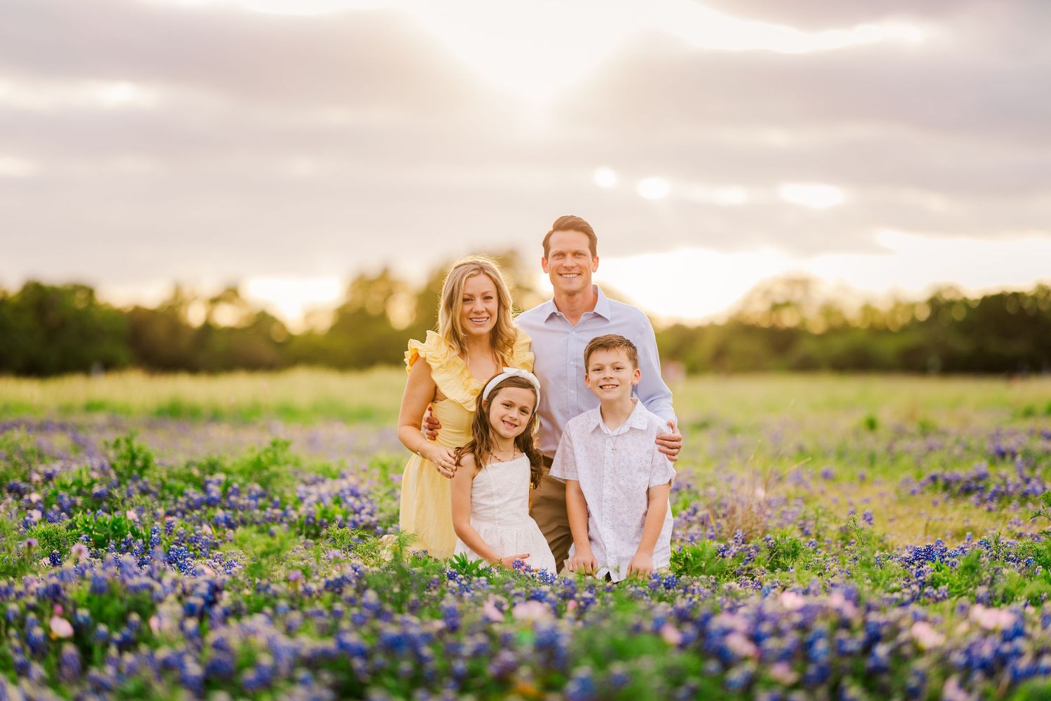 Family of four sitting in blooming bluebonnets during a Central Texas spring mini session with natural light photography.