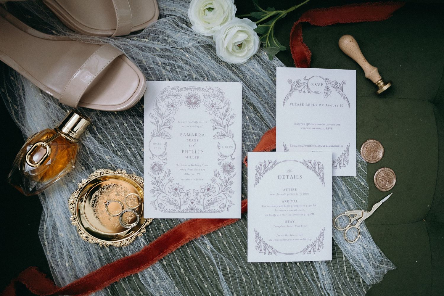 Wedding invitation suite displayed with champagne and white ranunculus flowers on a gray textile background.