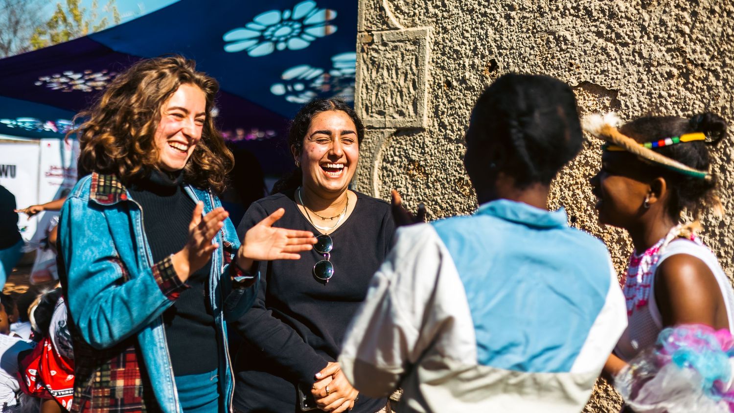 A diverse group of students interact and socialize in an outdoor campus setting on a sunny day.