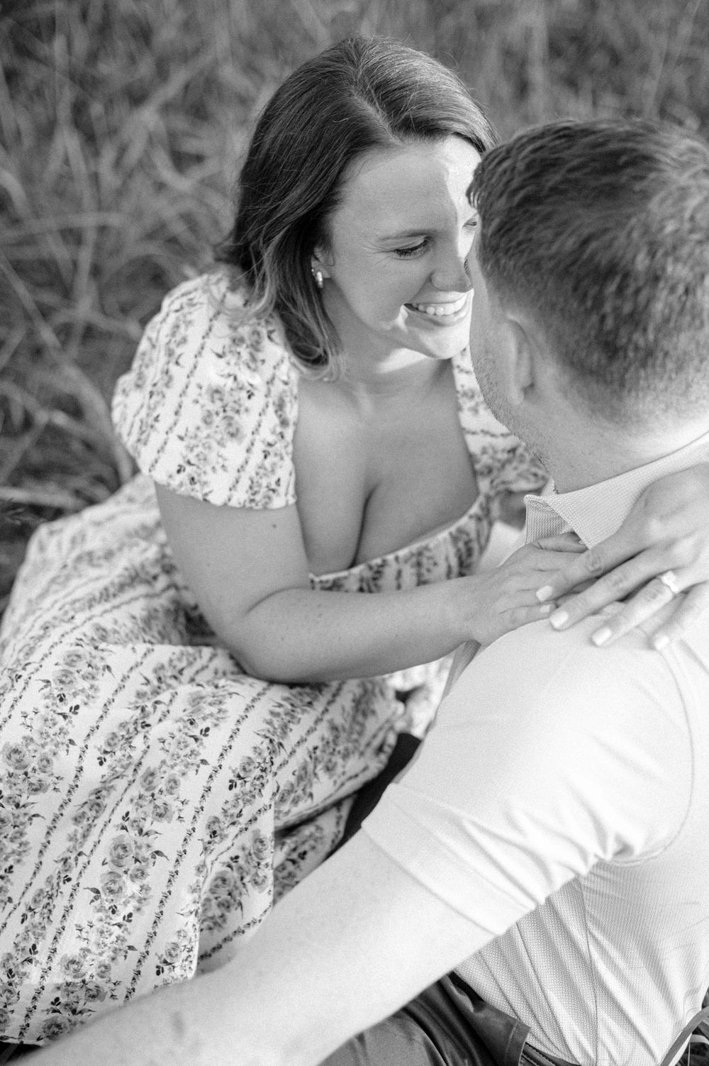 A romantic black and white portrait of a couple sharing an intimate moment while sitting in a grassy field.